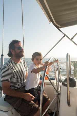 Man and boy holding steering wheel on yacht on water