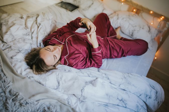 Woman lying down on bed with smartphone