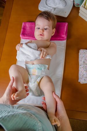 Cute baby playing with towel while father changes diaper
