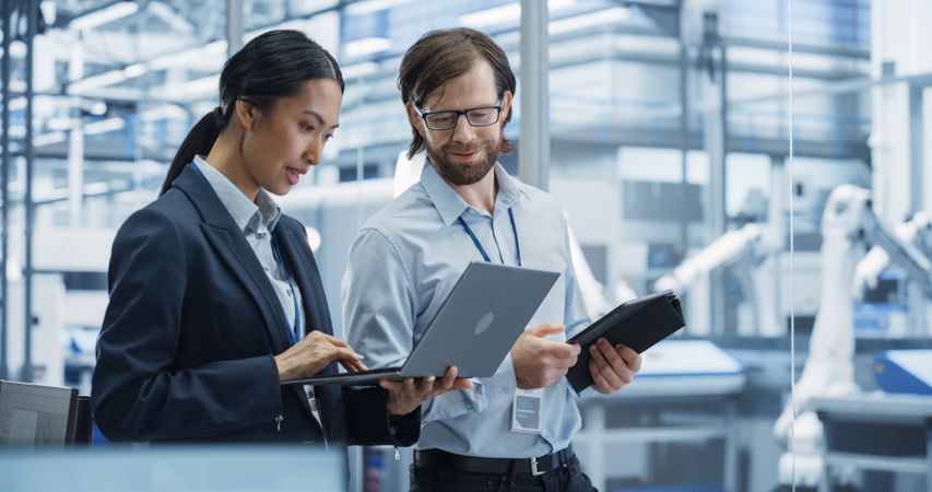 Industrial Engineers Working at Technology Factory. Man and Asian Female Using Laptop and Tablet Computers and Having a Conversation. Footage with a Portrait of a Couple of Employees