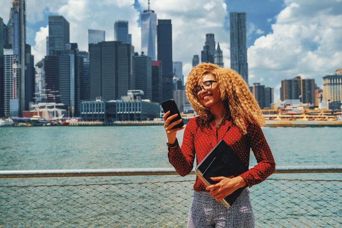 Happy professional Black female checking phone by Hudson River