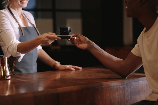 Barista handing customer a coffee over a wooden counter