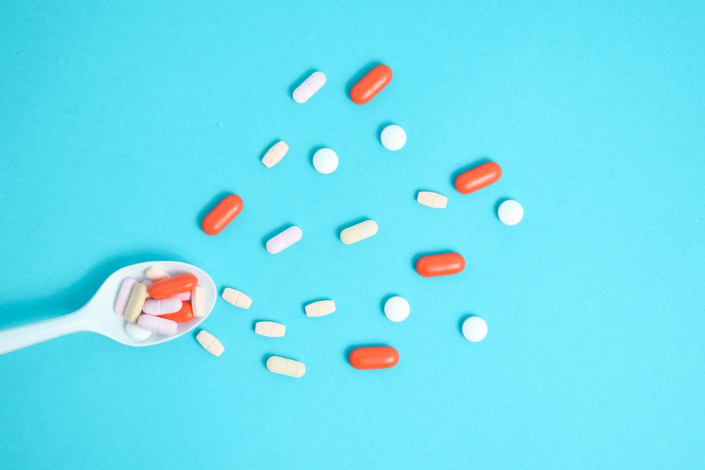 Scattered pills with plastic spoon on blue table