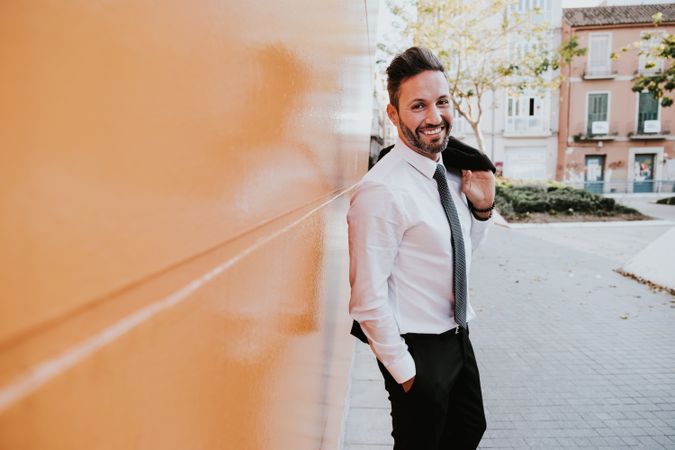 Adult smiling stylish man in costume near orange wall on street