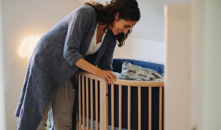 Woman looking at her baby in crib and smiling down at him