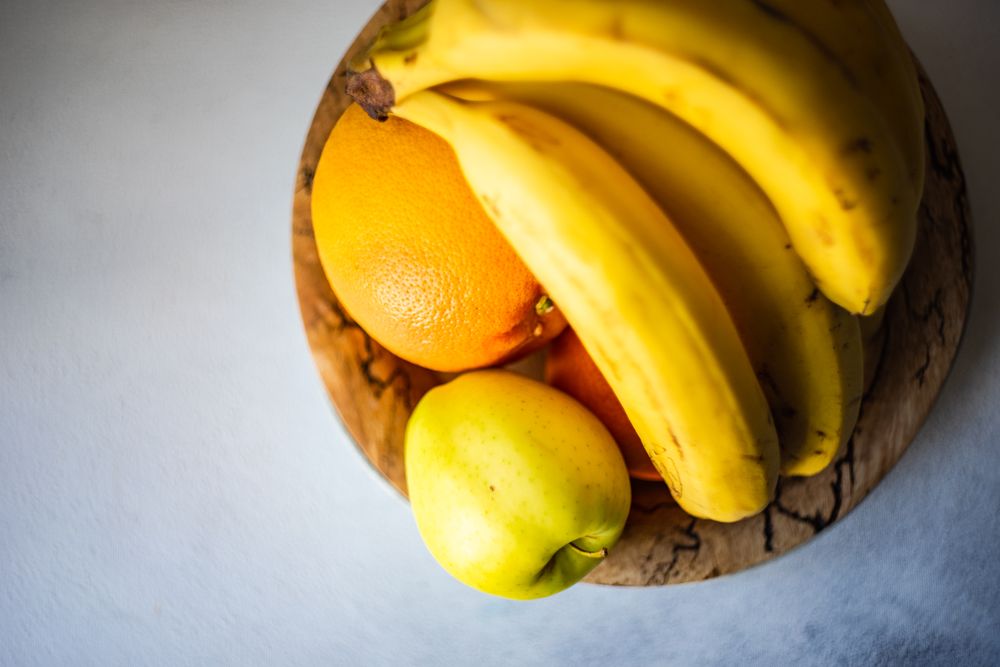 Top view of bowl of fruit with oranges, apple and bananas