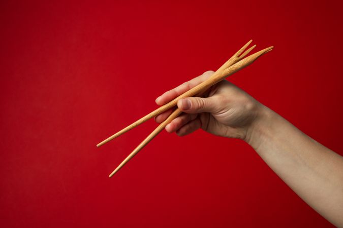Female hand with chopsticks on red background, close up
