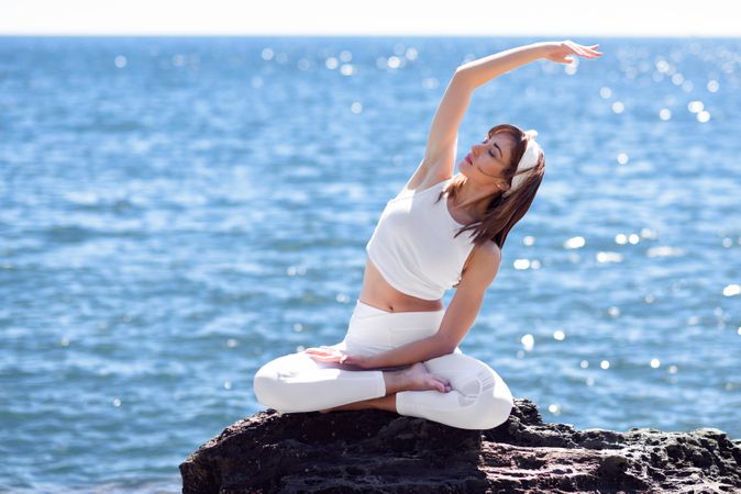 Female stretching her side in lotus pose on rocky beach