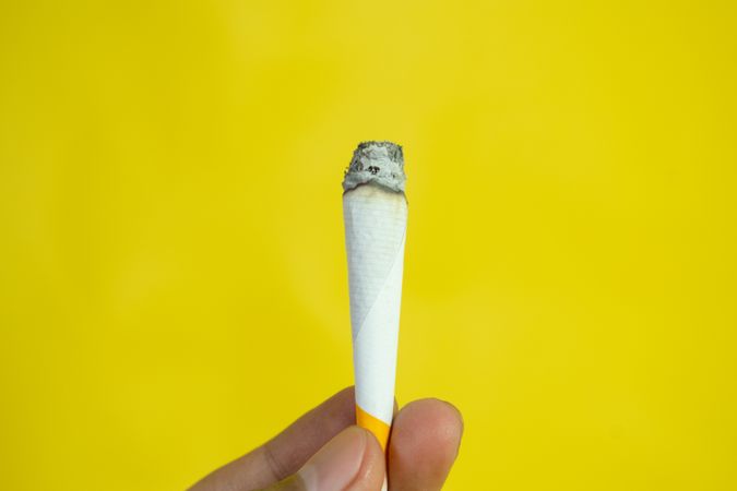 Yellow background with fingers holding burning hand rolled cigarette