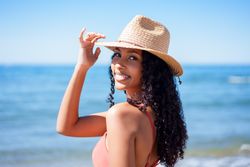 A Smiling Woman Wearing a Straw Hat, Enjoying a Beautiful Day at the Beach with Joy