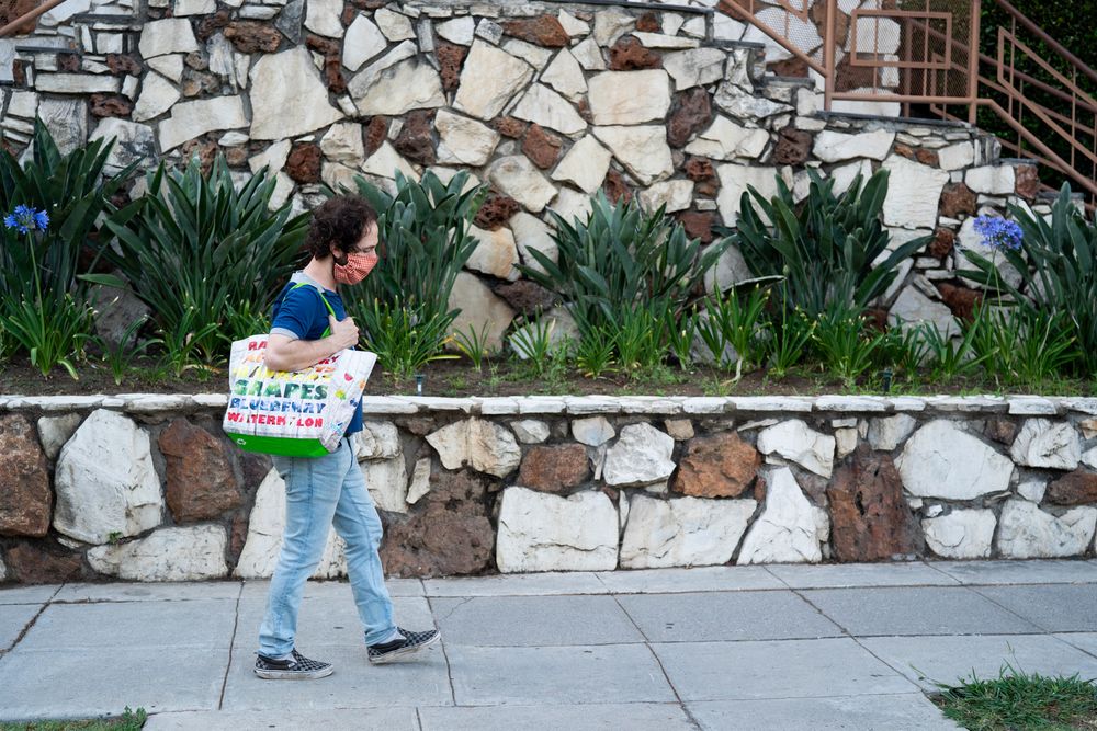 Full length side view of man walking in front of stone building with grocery tote