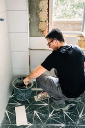 Mason taking cement from bucket to lay bathroom tiles