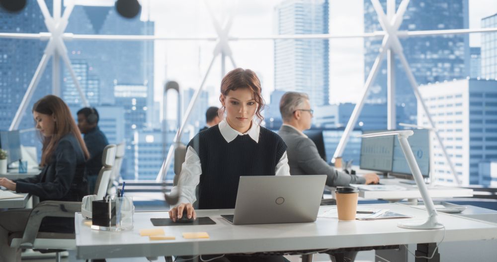 Female Business Development Manager Writing Emails In Workspace With Diverse Colleagues.