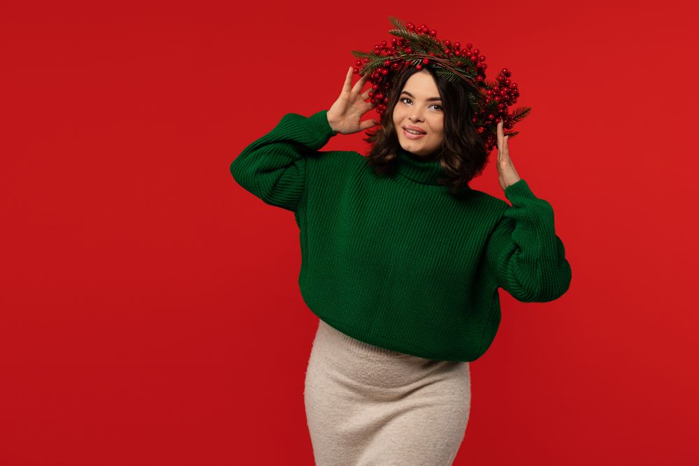 Smiling woman adjusting Christmas wreath of red berries on head.