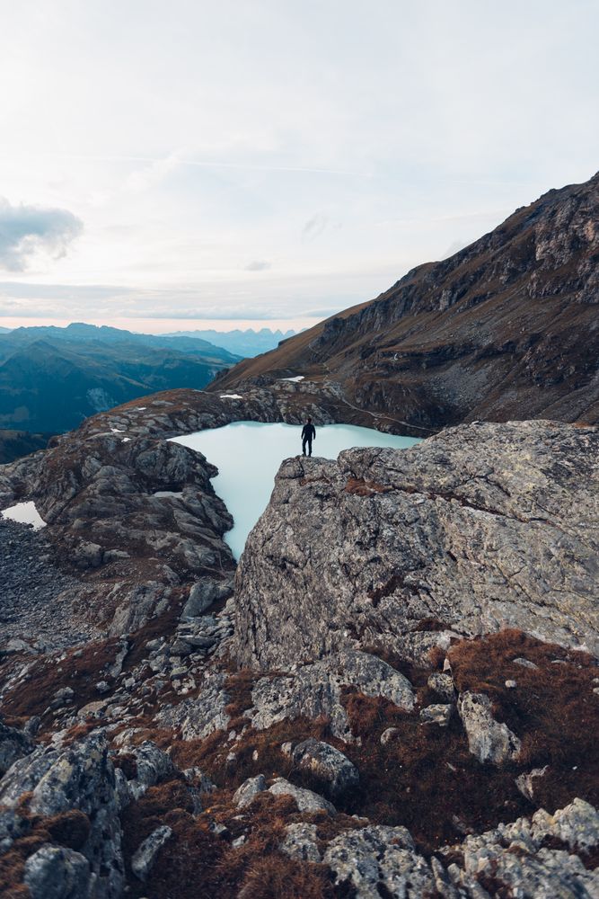 Man standing on rock formation on waterside of frozen lake in the mountain