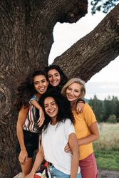 Four smiling woman posing in front of tree outside