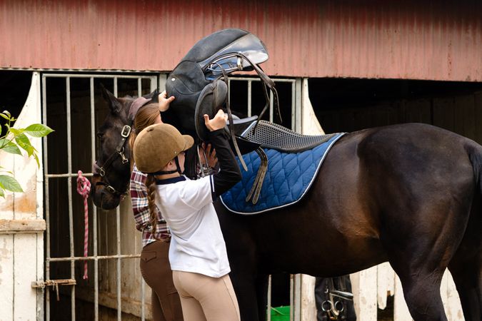Instructor and girl placing saddle on horse