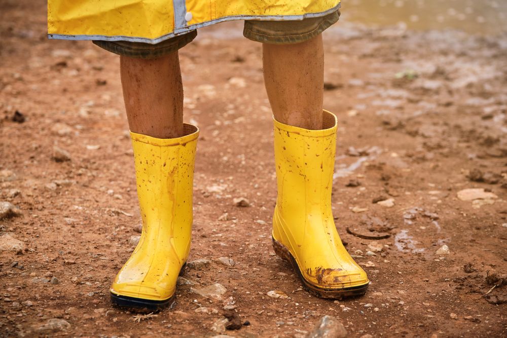 Crop child wearing yellow raincoat and standing in mud