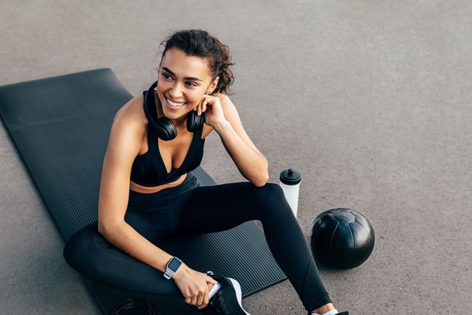 Smiling healthy woman sitting on exercise mat with headphones