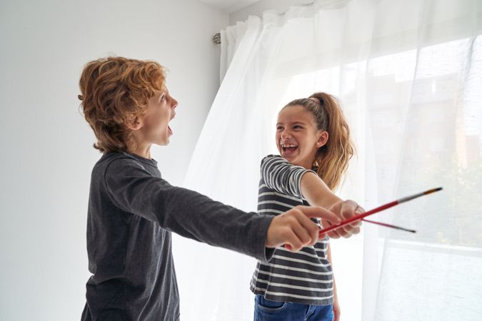 Joyful siblings playing in paintbrushes