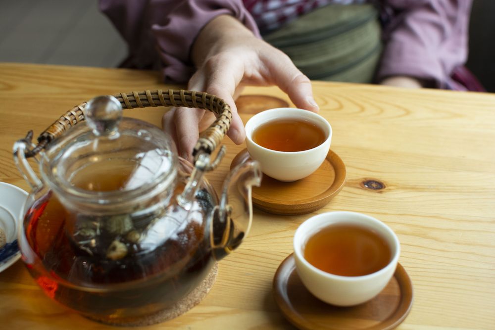 Person in kimono approaching cup of tea on wooden table