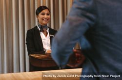 Smiling hotel receptionist attending guest at check-in counter 432gZ1