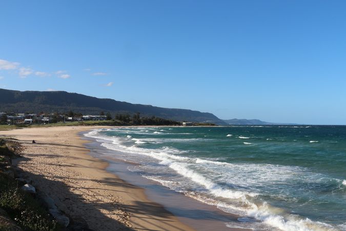 Scenic coastal view featuring golden sand and turquoise waves under a clear blue sky during daytime