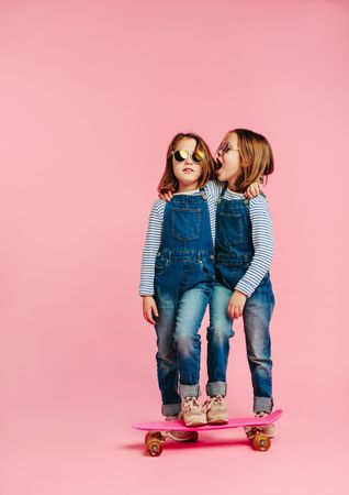 Twin girls wearing fashion clothes with skateboard on pink background