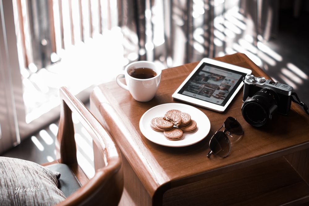 Tablet computer beside camera and cup of tea on wooden table