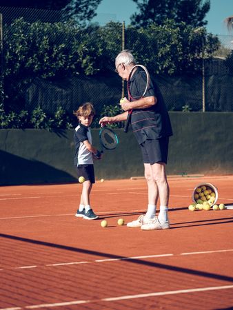 Older trainer explaining preteen boy with tennis racket techniq