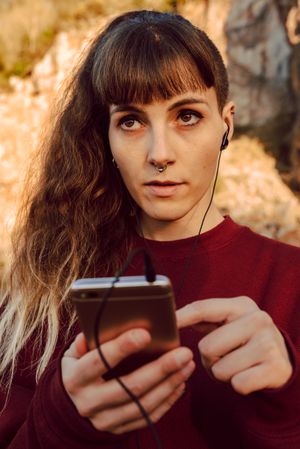Young woman with piercing listening music on smartphone on hill