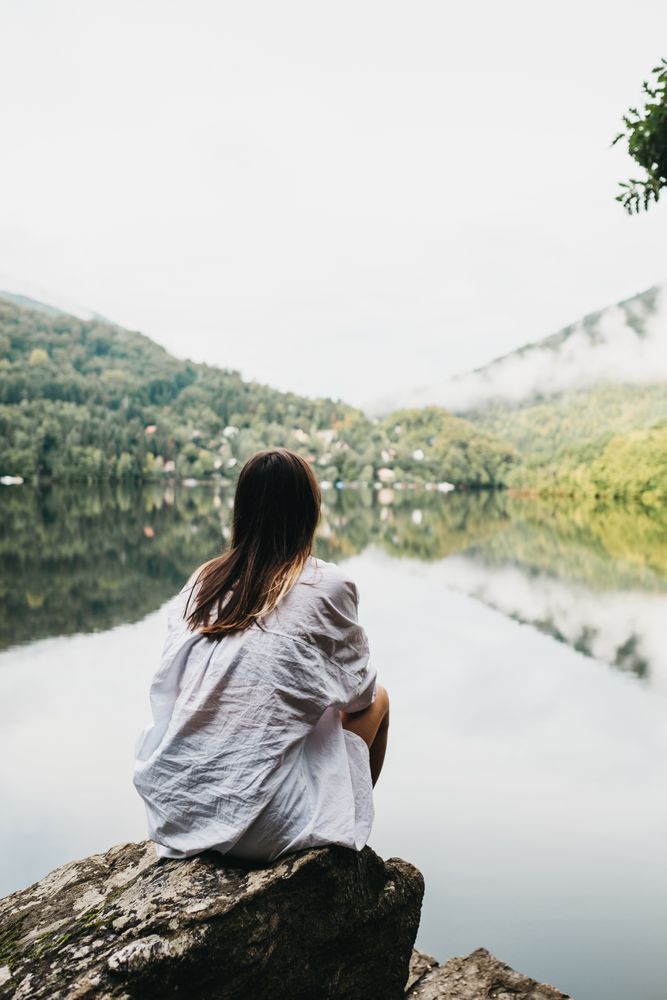 Woman sitting on rock near lake and mountains