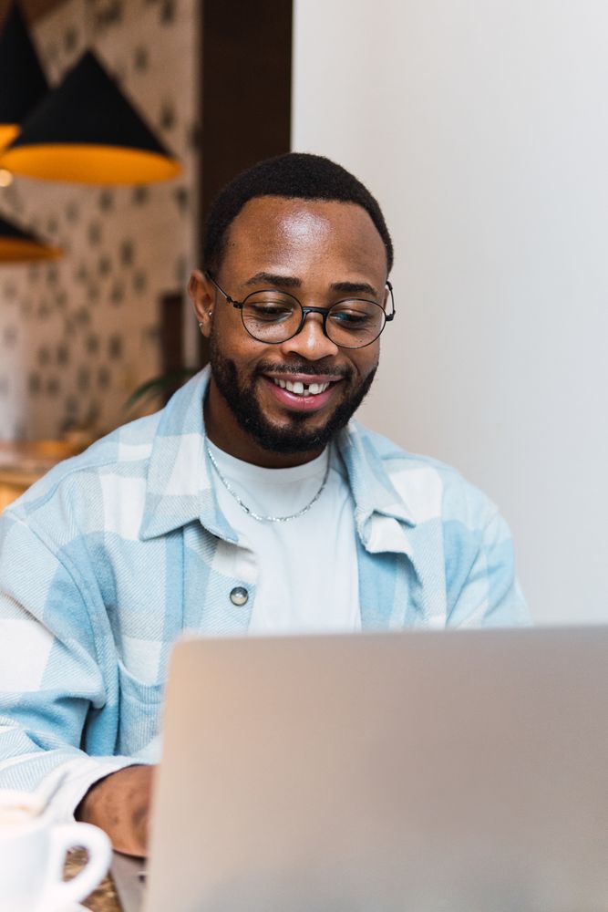 Delighted Black man with coffee browsing laptop