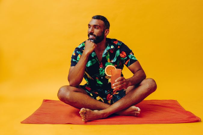 Black male looking away from camera and sitting on towel with tropical drink
