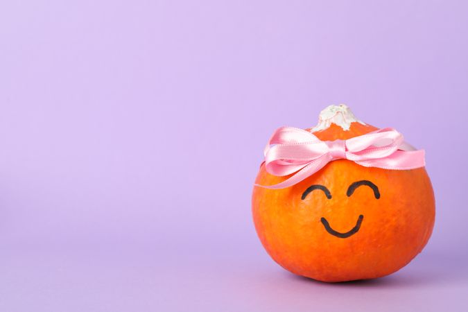 Pumpkin with smile and bow on violet background, space for text