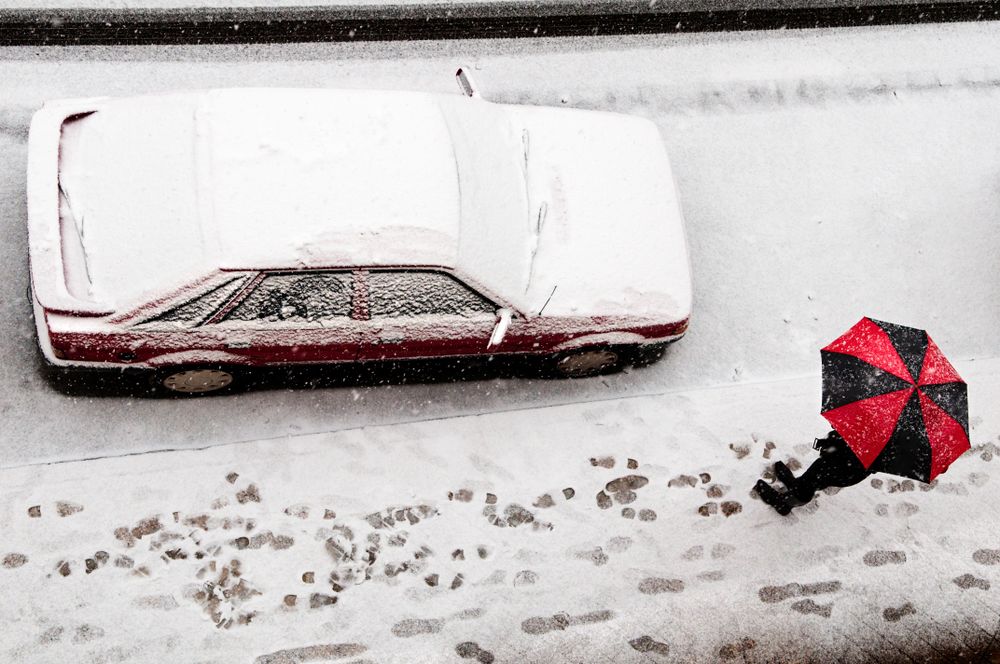 Top of red and dark umbrella shielding person from snowfall walking on street