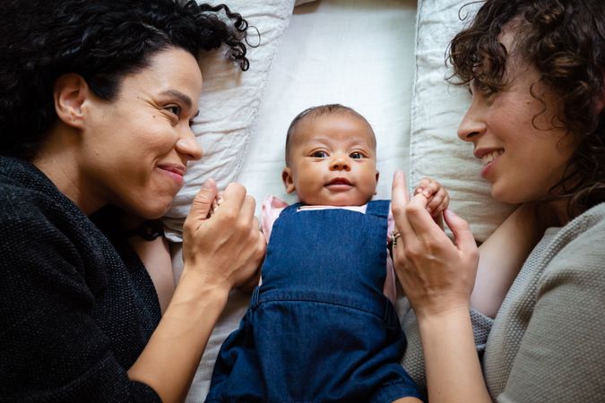 Two happy moms smiling and lying with cute baby on the bed