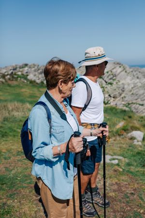 Mature man and woman with poles hiking outdoors, vertical