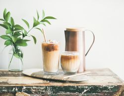 Two glasses of iced coffee glasses and a pitcher, with light background with leaves, square crop