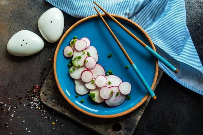 Top view of sliced radishes served with chopsticks on blue plate