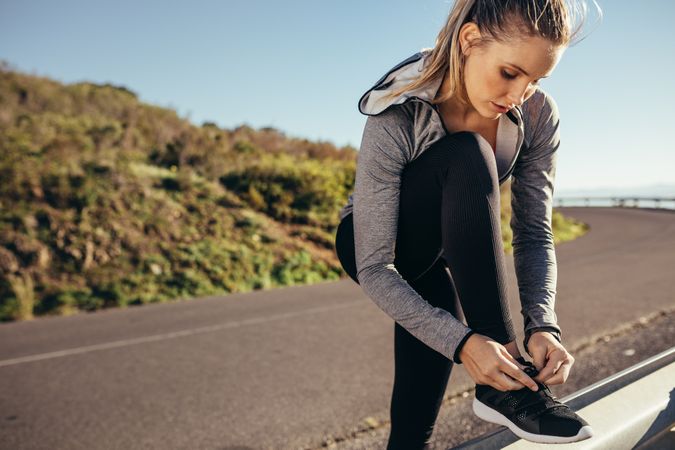Woman runner tying her shoelace standing on road