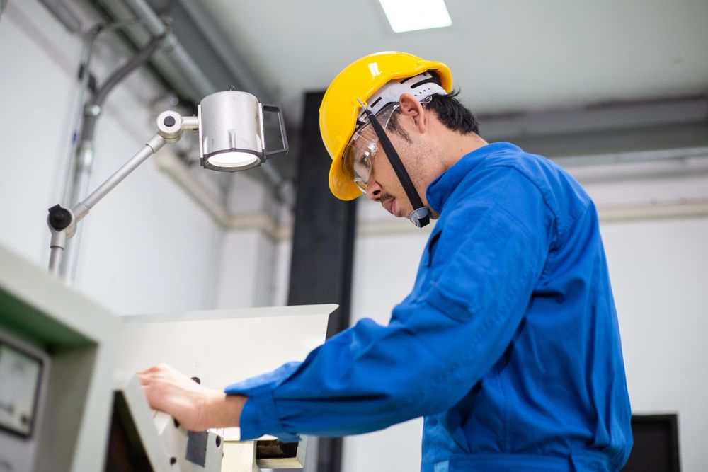Side view of Asian man in blue jumpsuit and yellow hard hat working in manufacturing