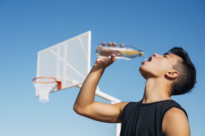Young man playing on basketball court outdoor drinking water