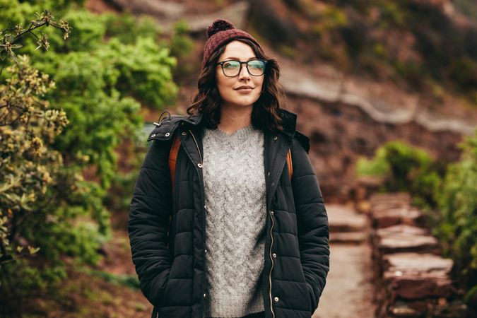 Woman traveler in warm clothing with eyeglasses looking away at landscape from mountain