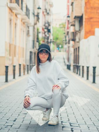 Young trendy woman sitting against street