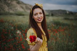 glad adult woman holding rose and looking at camera while standing in meadow