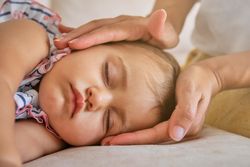 Faceless mother protecting daughter sleeping on sofa