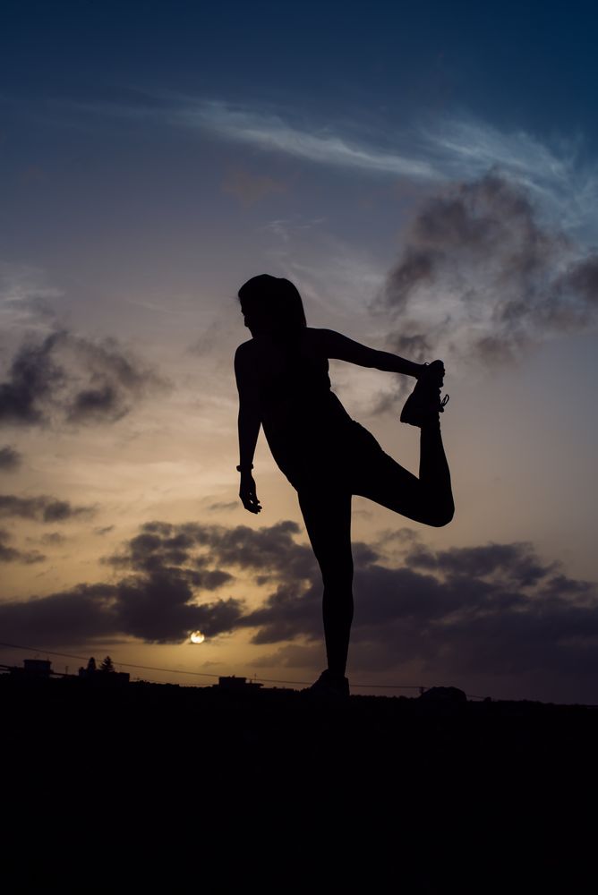 Stretching woman and sky with clouds at sunset