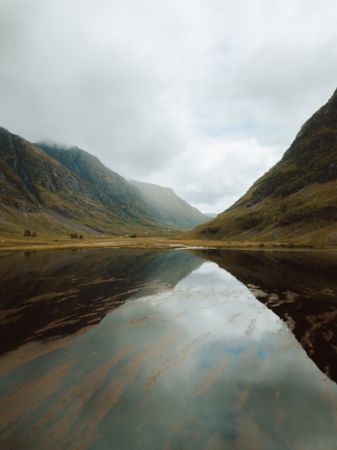 Tranquil lake amidst hills on cloudy day