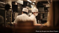 Two restaurant chefs with facemasks in the kitchen 476WP5